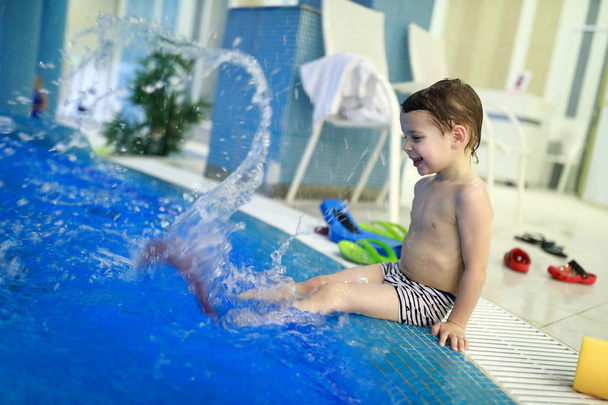 Boy in flippers sitting on edge of pool - Zdjęcie, obraz