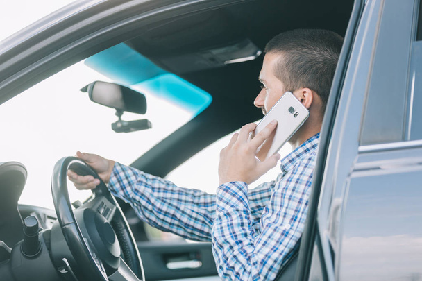 man talking on a smartphone, sitting behind the wheel of a car. - Фото, зображення