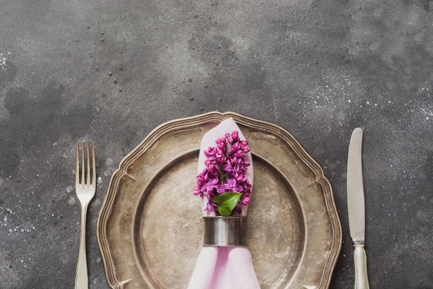 Spring elegant table place setting with violet lilac flowers, silverware on dark table. Top view. - Foto, Imagem