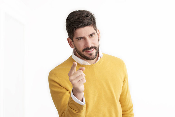 handsome Caucasian man wearing yellow sweater and posing at white background and pointing finger on camera  - Foto, Bild