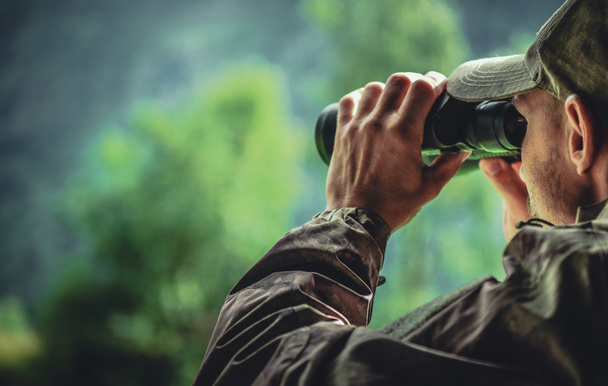Caucasian Hunter in Camouflage with Binoculars Spotting Wildlife in the Remote Place (en inglés). Tema de caza
. - Foto, imagen