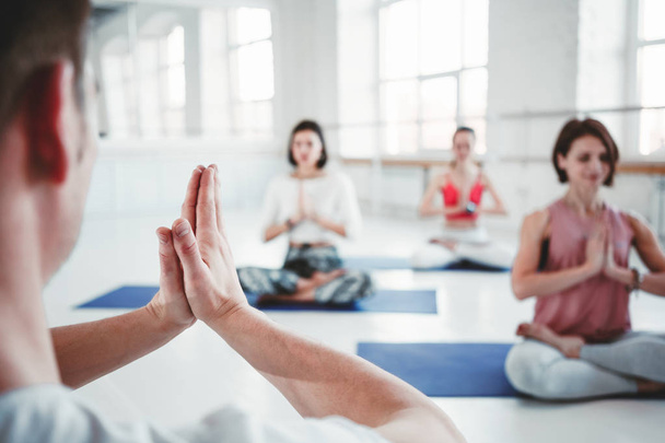 Group of adult women and man doing yoga exercises together in fitness class. Active people practice yoga poses on mat. Health care and lifestyle. Blurred background - Photo, Image