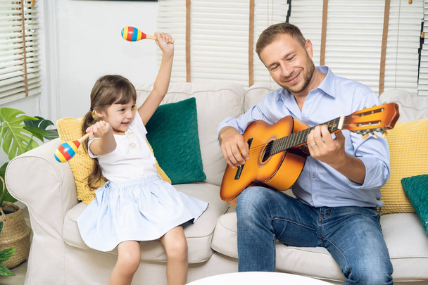 Mutlu babalar günü. Gülümseyen baba gitar ve kızı dans ve evde kanepe, etkinlik aile sevgi ve liftstyle kavramı oturan Marakas tutan oynarken komik portresi - Fotoğraf, Görsel