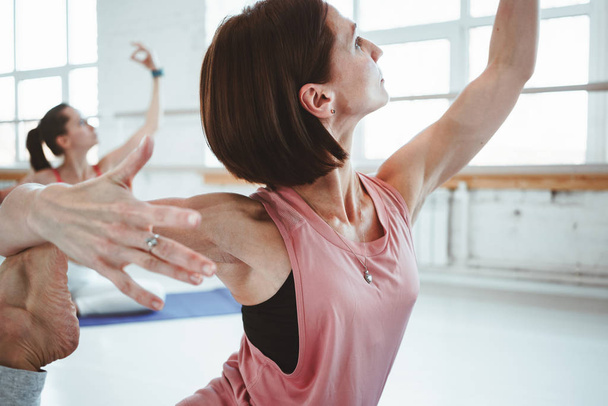 Strong adult woman practicing yoga poses for maintaining health care. Group of active females doing fithess stretching exercises together indoor class. Blurred background - Fotoğraf, Görsel