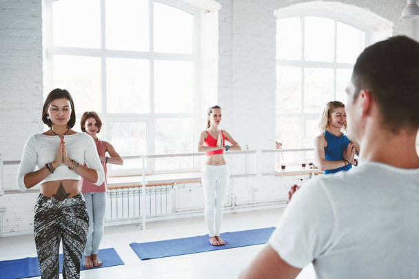 Adult man yoga instructor trains and teaching group of women yoga exercises for maintaining health care in white class. Lifestyle concept - Valokuva, kuva