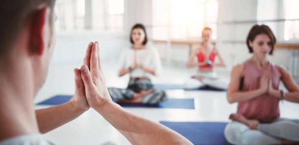 Man coach trains group of women yoga exercises for maintaining health care in white class. People together practis yoga poses. Wide - Fotoğraf, Görsel