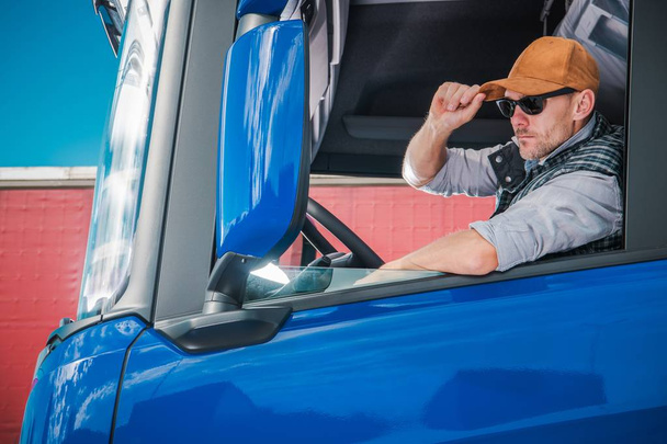 Joven conductor de camión caucásico con sombrero de béisbol dentro de la cabina semi
. - Foto, Imagen