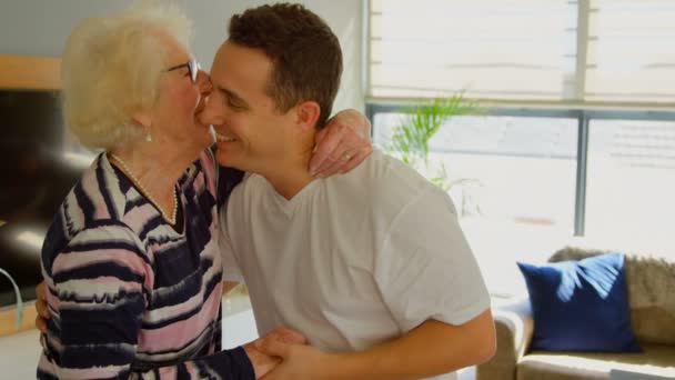 Adult son kissing his elder retired mother. Family standing dancing in living room at home. - Felvétel, videó