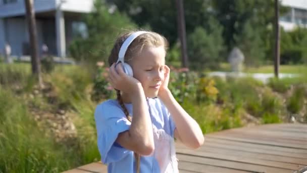 Little adorable girl słuchanie muzyki w parku - Materiał filmowy, wideo