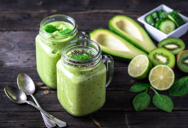 Green smoothie on dark background with avocado, spinach, lemon and kiwi on the right side. - Foto, imagen