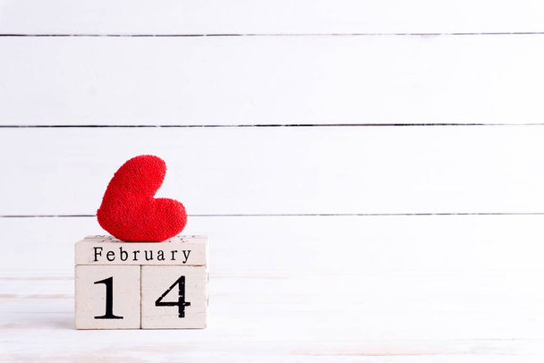 Concepto de San Valentín. 14 de febrero texto en bloque de madera con corazón rojo hecho a mano sobre fondo de madera blanca
. - Foto, imagen