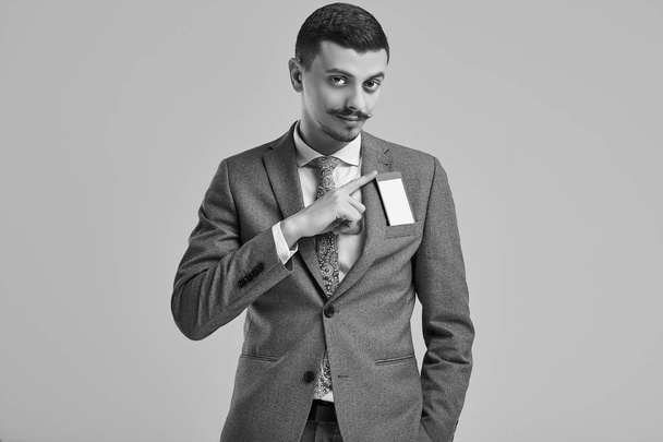 Portrait of handsome young confident arabic businessman with fancy mustache in fashion gray full suit hiding the phone in his pocket on studio background - Photo, Image