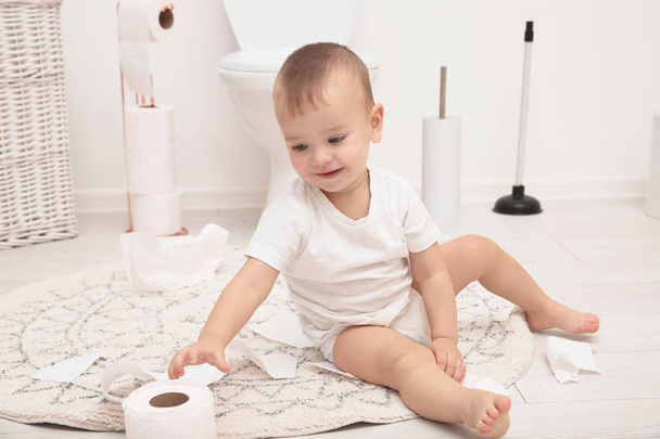 Cute toddler playing with toilet paper in bathroom - Fotó, kép