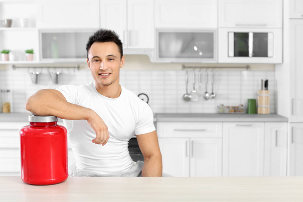 Man with jar of protein shake powder in kitchen. Space for text - Zdjęcie, obraz