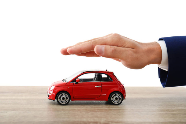 Insurance agent holding hand over toy car on table against white background, closeup - Foto, Imagem