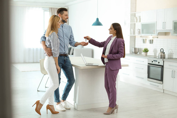 Female real estate agent giving house key to couple indoors - Foto, immagini