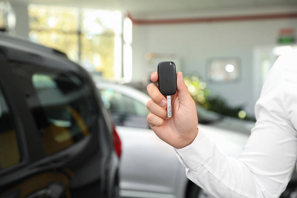 Young man with car key in dealership, closeup - Фото, зображення