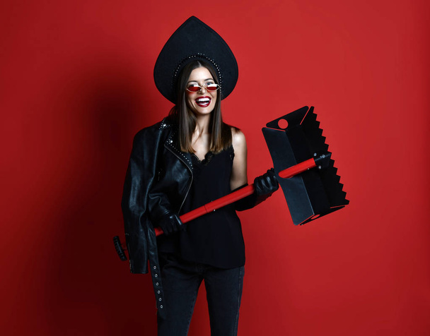 Woman hold portable shovel spade in black leather jacket in high fashion sunglasses on red - Φωτογραφία, εικόνα