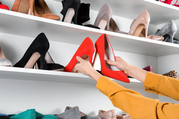 Mujer tomando zapatos de tacón alto de la unidad de estanterías, primer plano
 - Foto, Imagen