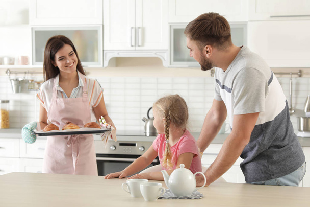 Young beautiful woman treating her family with freshly oven baked buns in kitchen - Zdjęcie, obraz