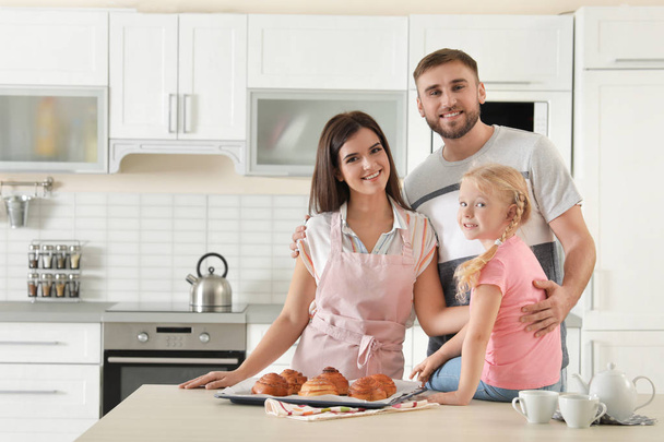 Happy family with tray of freshly oven baked buns at table in kitchen. Space for text - Zdjęcie, obraz