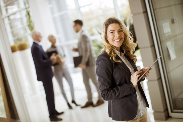 Porträt einer jungen Geschäftsfrau mit Tablet im Büro, während sich andere Geschäftsleute im Hintergrund unterhalten - Foto, Bild