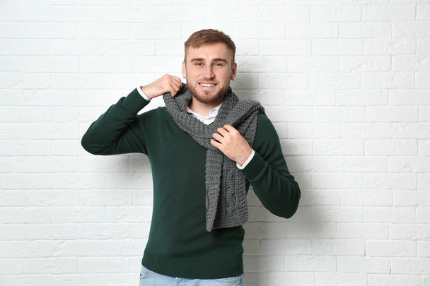 Handsome young man in warm sweater with scarf near white brick wall - Fotoğraf, Görsel