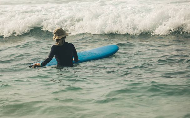 nainen surffaaja kanssa surffilauta vedessä katsomalla tulevina aaltoina
 - Valokuva, kuva