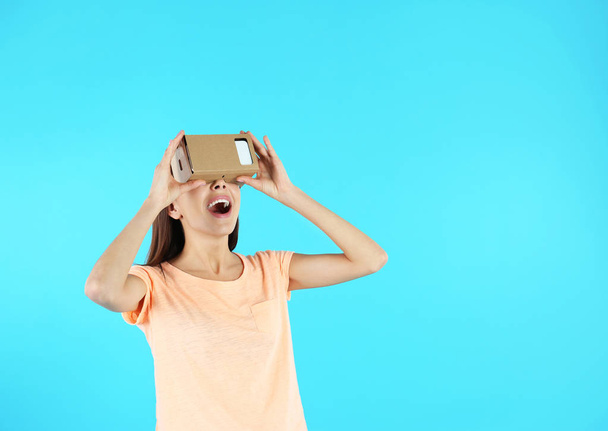 Young woman using cardboard virtual reality headset on color background. Space for text - Fotografie, Obrázek
