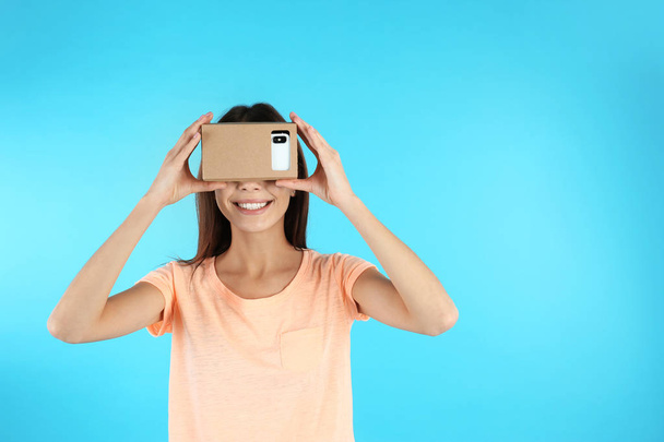 Young woman using cardboard virtual reality headset on color background. Space for text - 写真・画像