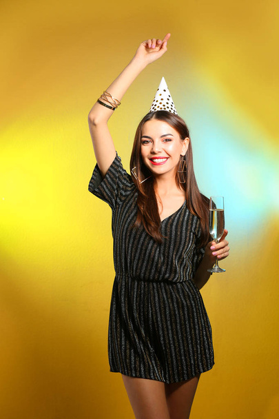 Portrait of happy woman with party hat and champagne in glass on color background - Φωτογραφία, εικόνα