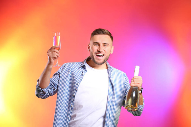 Portrait of happy man holding bottle and glass with champagne on color background - Fotoğraf, Görsel