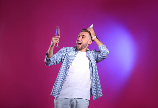 Portrait of happy man with party cap and champagne in glass on color background - Foto, immagini
