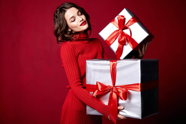 Beautiful young pretty woman with a bright evening make-up of shiny red lipstick on the lips brunette curly hair festive mood knitted red sweater winter Christmas New Year and birthday gift surprise. - Foto, Bild