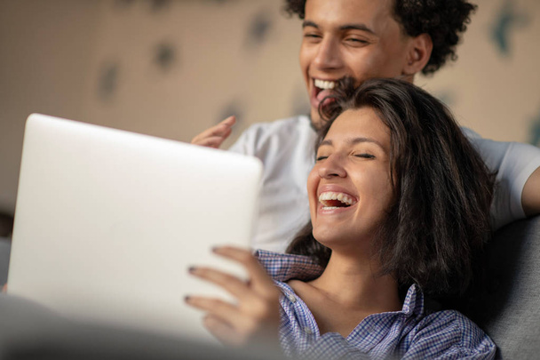 家の内部にラップトップ コンピューター上のムービーを見ながら笑っている陽気な幸せなアフリカ系アメリカ人若年層の結婚. - 写真・画像