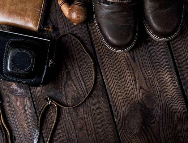 pair of leather brown shoes and an old vintage camera in a case on a wooden background, copy space - 写真・画像