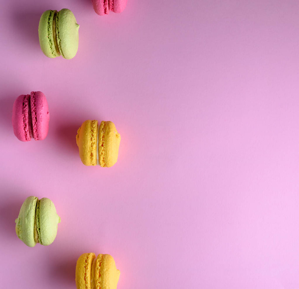 torte multicolori di farina di mandorle con crema si trovano in fila su uno sfondo rosa, spazio copia
 - Foto, immagini