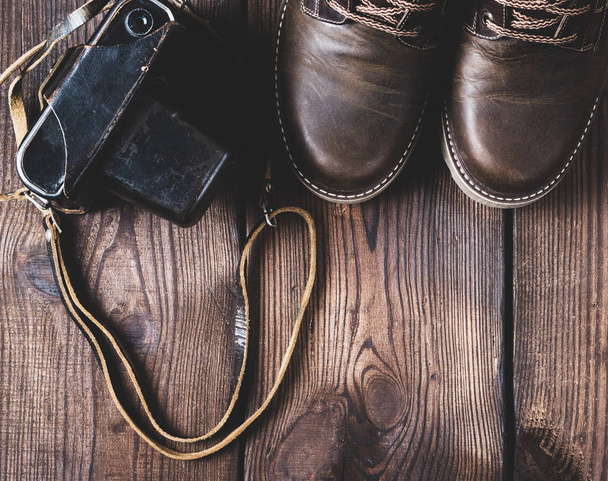pair of leather brown shoes and an old vintage camera in a case on a wooden background, empty space - Foto, Imagen