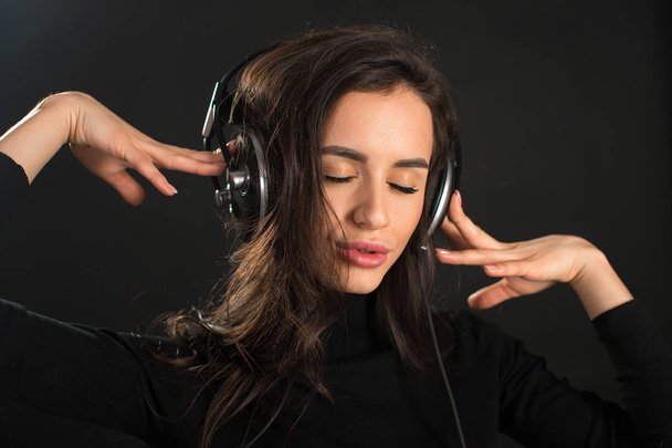 Mooie genieten van jonge vrouw luisteren van de muziek in draadloze hoofdtelefoon met gesloten ogen op donkere zwarte achtergrond. Closeup - Foto, afbeelding