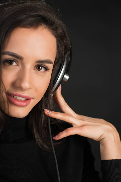 DJ девушка в наушниках слушает диско бьет позировать в студии на темном фоне. Молодая привлекательная кавказская женщина-модель развлекает людей
. - Фото, изображение