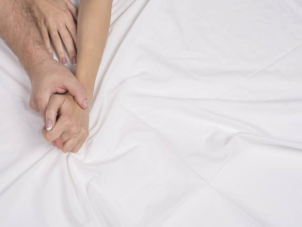Close-up de mãos de casal deitar na cama no quarto, os amantes têm sexo intenso ou fazer amor sentindo orgasmo e satisfação, namorado e namorada desfrutar de preliminares em lençóis brancos
. - Foto, Imagem