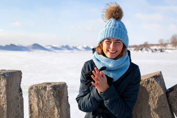 Portret uroda kobieta model na tle zimy. Piękny nowoczesny miejski młoda kobieta kapeluszu niebieski dziania basks w zimnie na tle morza mrożone - Zdjęcie, obraz