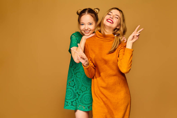 Two young beautiful blond smiling hipster girls posing in trendy summer clothes. Carefree women isolated on golden background. Positive models going crazy and hugging - Foto, Imagem