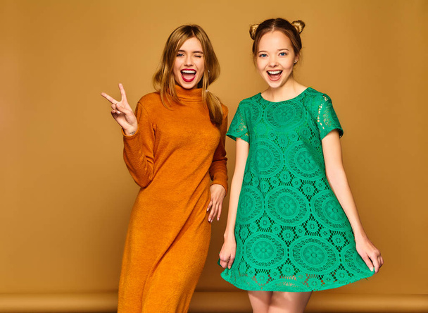 Two young beautiful blond smiling hipster girls posing in trendy summer clothes. Carefree women isolated on golden background. Positive models going crazy  - Φωτογραφία, εικόνα