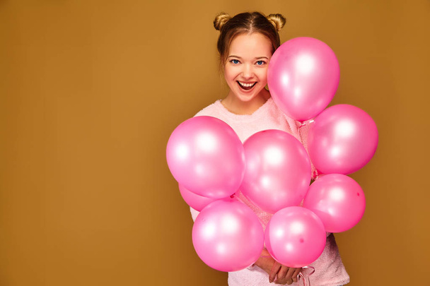 Excited young girl in white cute clothes. Woman model with pink air balloons on golden background. St. Women's Day; Happy New Year; birthday holiday party - Foto, afbeelding