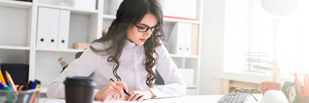 Una joven se sienta en la mesa de la oficina, sostiene un bolígrafo en la mano y mira los documentos
. - Foto, imagen