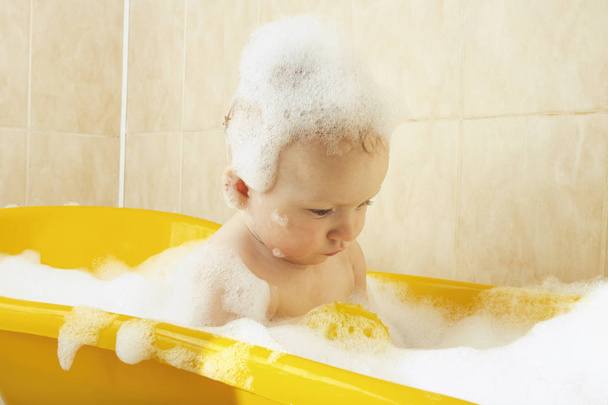 Pequeno bebê toma um banho em um banho amarelo com bolhas e espuma. O conceito de criança feliz, amor para tomar banho - Foto, Imagem