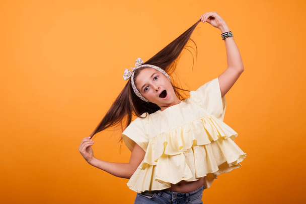 Little girl playing with her hair on a photoshoot in studio on yellow background - Foto, Bild