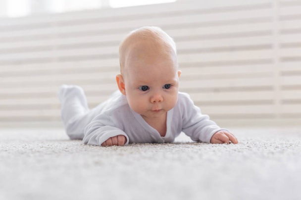 παιδική ηλικία, άνθρωποι και αχρωμικές έννοια - μικρό μωρό αγόρι ή κορίτσι που σέρνεται στο πάτωμα στο σπίτι - Φωτογραφία, εικόνα
