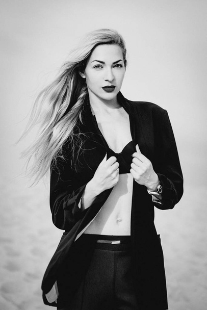 monochrome portrait of long blonde hair stylish, amazing, fashionable, modern white woman in black bra and suit outdoor in desert - Фото, зображення